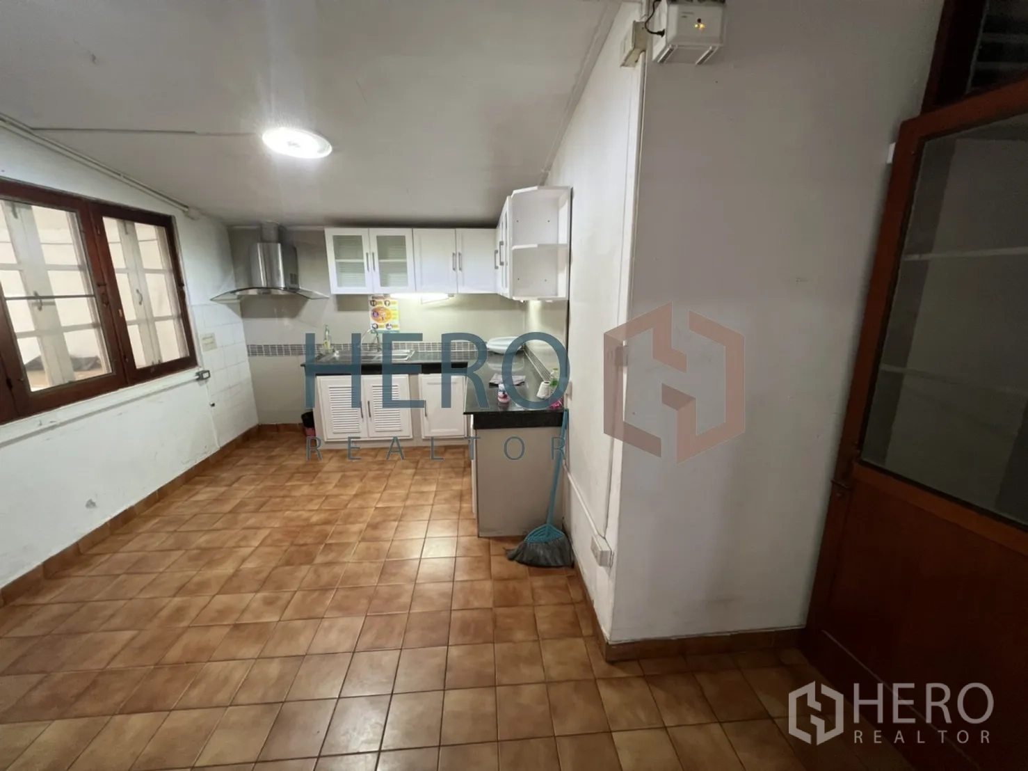 Detached House for rent in Watthana, Bangkok - Separate kitchen with upper cabinets, range hood and terracotta floor tiles.