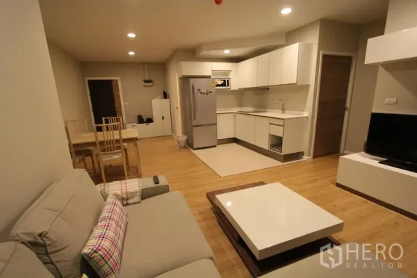 Condominium for rent in Pathum Wan, Bangkok - Open-plan living area showing sofa, dining set and a white L-shaped kitchen.