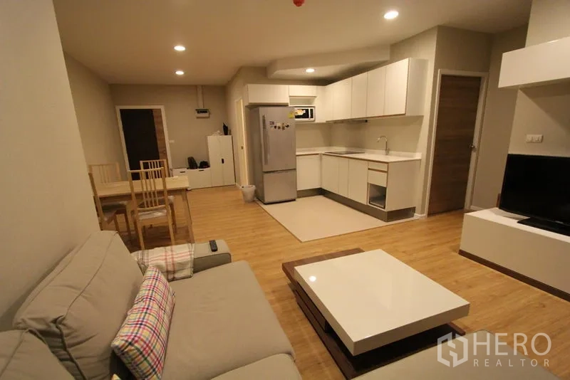 Condominium for rent in Pathum Wan, Bangkok - Open-plan living area showing sofa, dining set and a white L-shaped kitchen.
