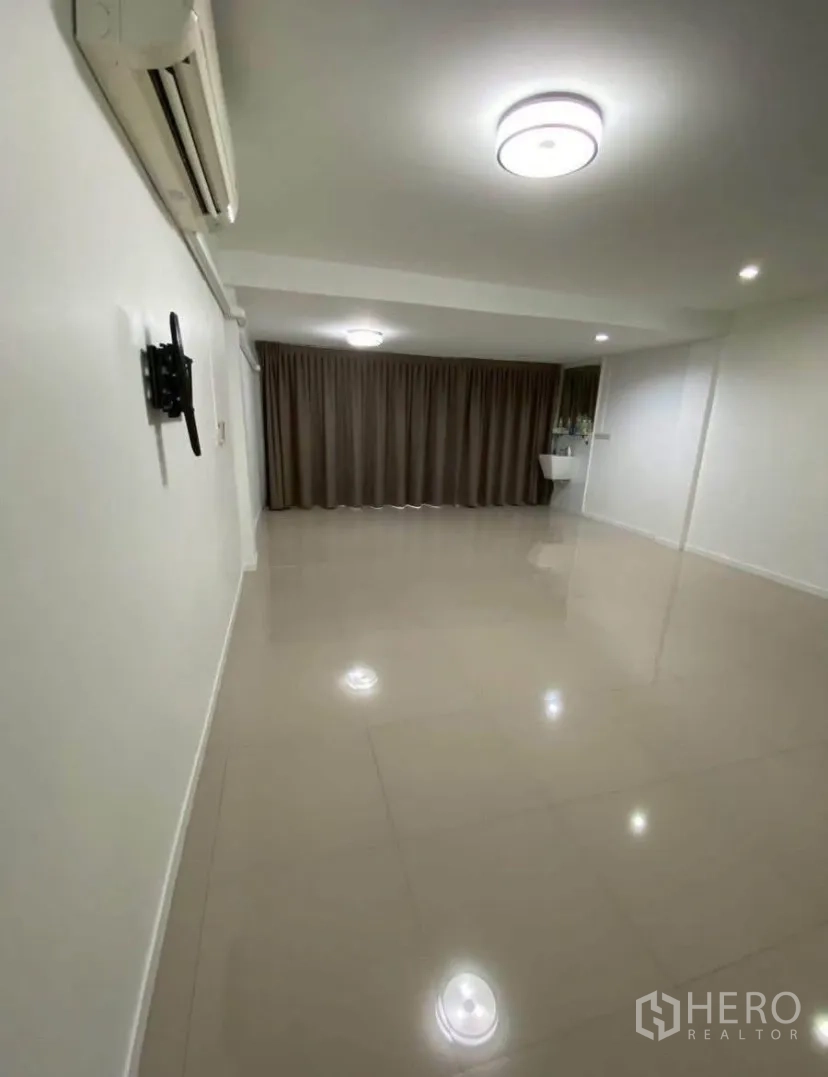 Townhouse for rent in Phra Khanong, Bangkok - Large tiled room with air conditioner, ceiling lights, and long curtains.