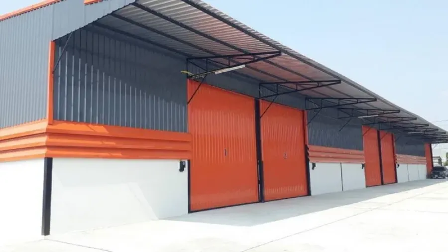 Warehouse for rent in Lam Luk Ka, Pathum Thani - Newly built warehouse exterior with bright orange steel sliding doors, long metal awning and wide concrete driveway.