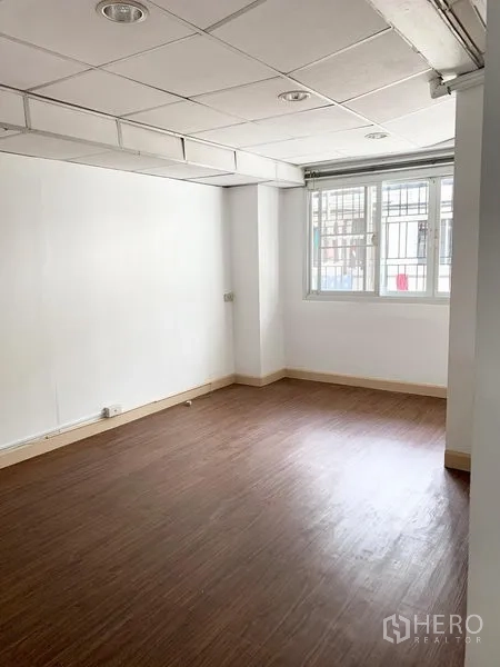 Townhouse for rent in Khlong Toei, Bangkok - Cozy bedroom with wood laminate flooring and a window fitted with security grilles.