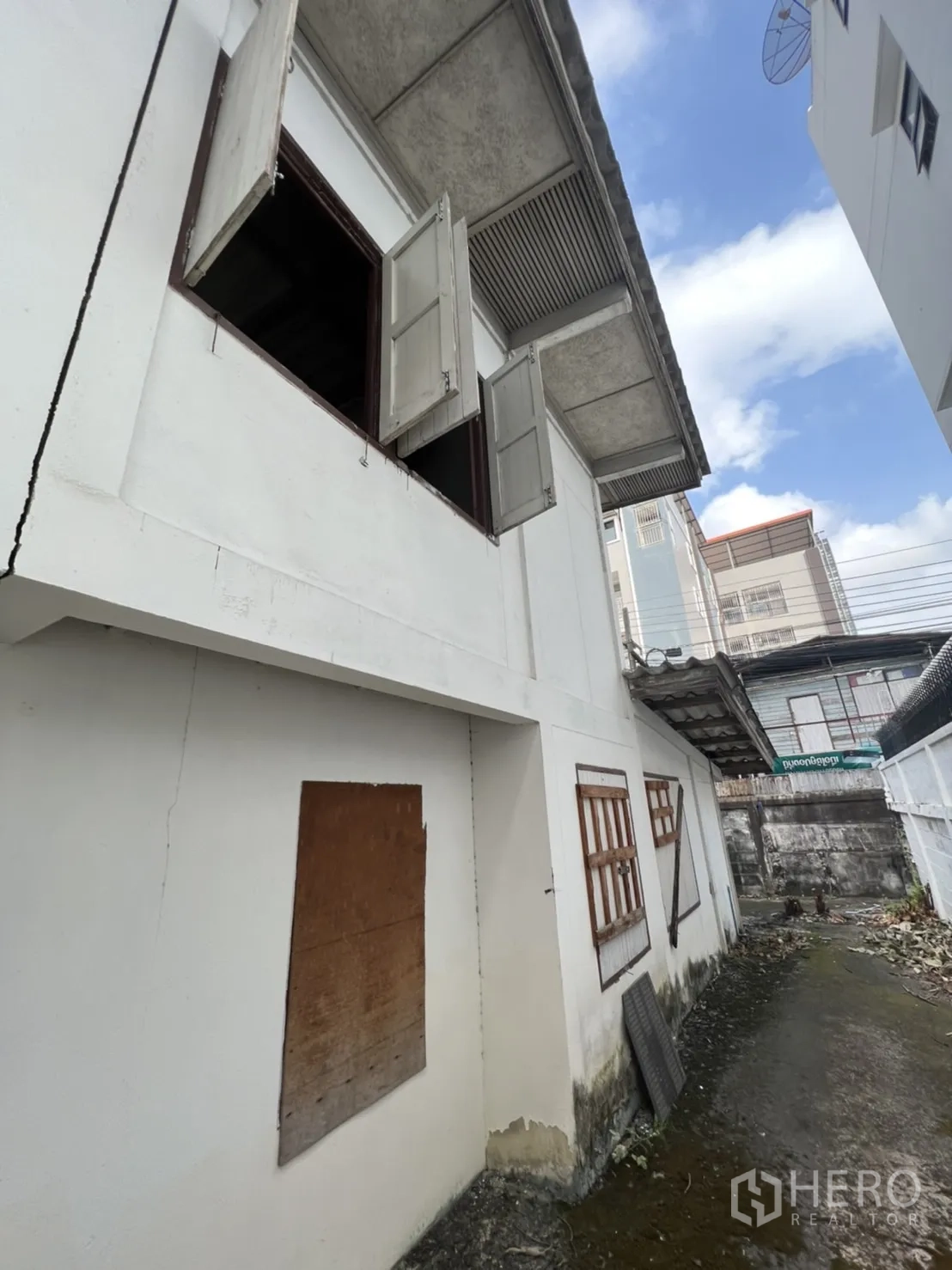 Detached House for rent in Sathon, Bangkok - Close-up of upper-floor windows and roofline of an older white house with city buildings in the background.