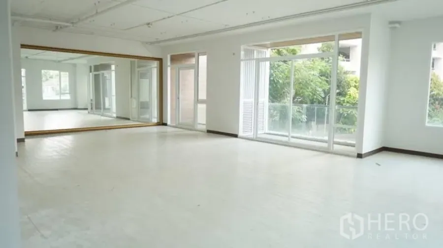 Retail Space for rent in Khlong Toei, Bangkok - Bright open retail studio with a full-length mirror wall, large windows and a balcony door facing greenery.
