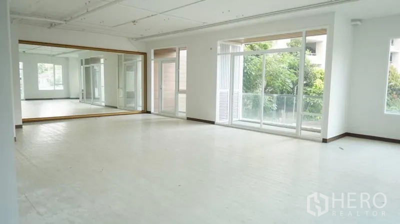 Retail Space for rent in Khlong Toei, Bangkok - Bright open retail studio with a full-length mirror wall, large windows and a balcony door facing greenery.