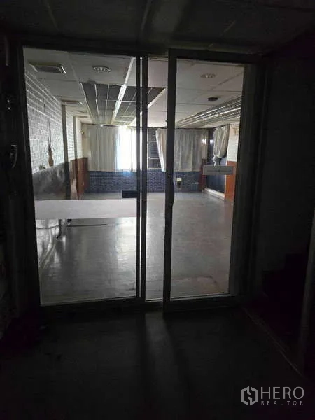 Shophouse for rent in Watthana, Bangkok - View through glass sliding door to large open room with window and ceiling grid.