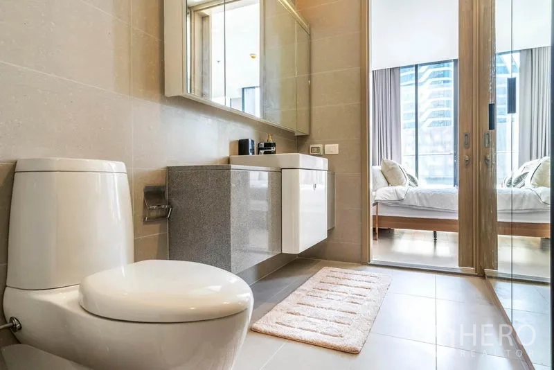 Condominium for rent in Pathum Wan, Bangkok - Bathroom view toward the bedroom with floating vanity, mirrored cabinet and toilet.