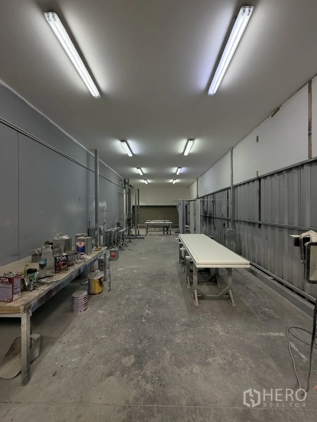 Factory for rent or sale in Lam Luk Ka, Pathum Thani - Enclosed finishing room with fluorescent lighting, tables, and paint cans.