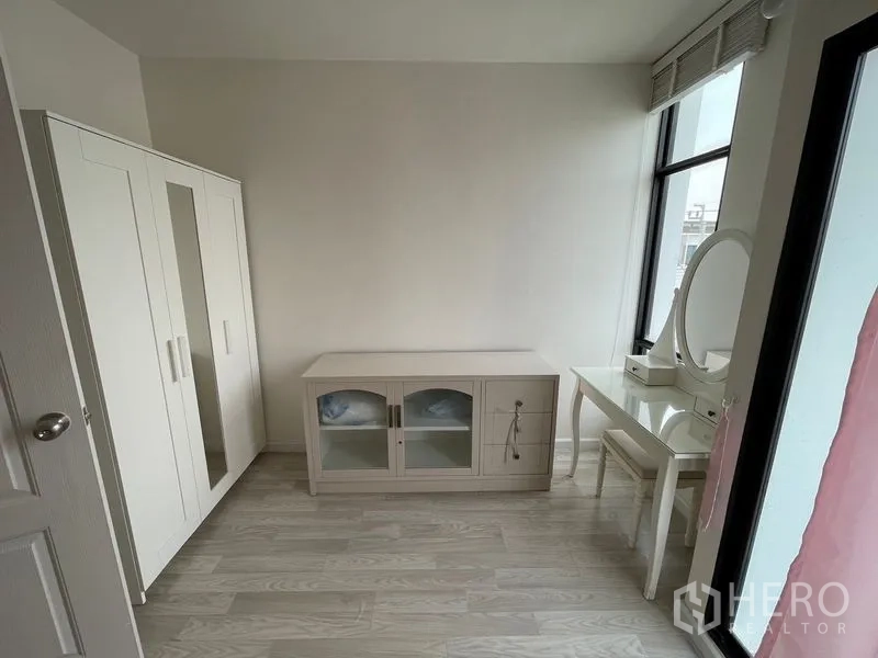 Townhouse for rent in Bang Kapi, Bangkok - Compact room with white wardrobe, vanity table and sideboard beside a tall window.