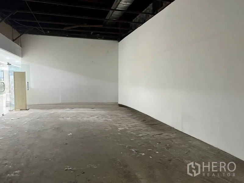 Retail Space for rent in Khlong Toei, Bangkok - Deep retail area with a long curved white wall and raw flooring.