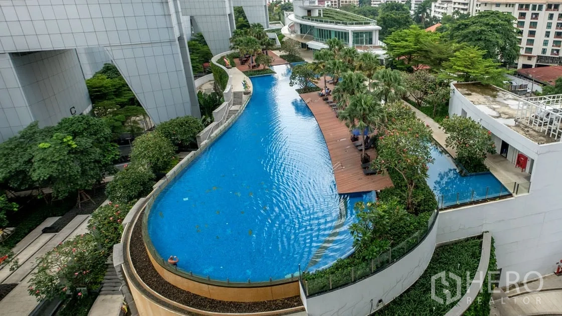 Condominium for rent in Khlong Toei, Bangkok - Lagoon-style outdoor swimming pool with timber deck, sun loungers and lush tropical gardens.