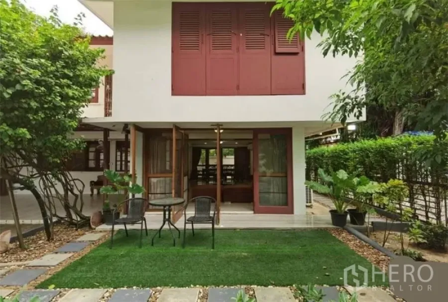 Detached House for rent in Watthana, Bangkok - Two-storey detached house with red shutters, patio doors to a lawn garden and outdoor seating.