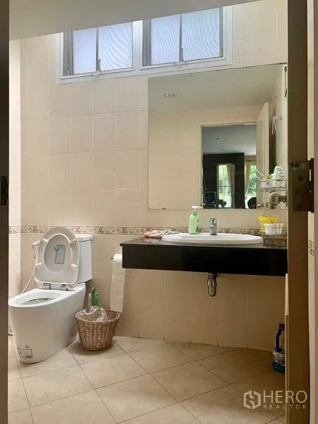 Detached House for rent in Prawet, Bangkok - Bright tiled bathroom with window, large wall mirror, and floating vanity.