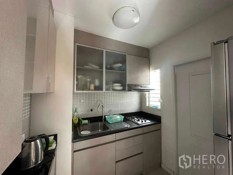 Home Office for rent in Chatuchak, Bangkok - Compact fitted kitchen with cabinets, sink, cooktop, and refrigerator.