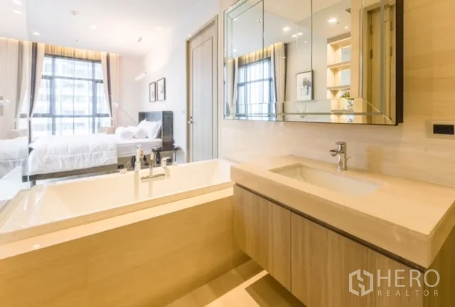 Condominium for rent or sale in Watthana, Bangkok - Contemporary bathroom with soaking tub, vanity and mirrored cabinets behind a glass partition.