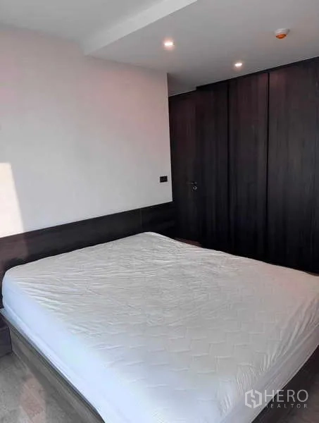 Condominium for rent in Khlong Toei, Bangkok - Bedroom with double bed and dark built-in wardrobes.