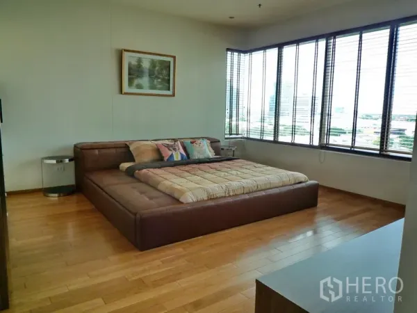 Condominium for rent in Khlong Toei, Bangkok - Spacious master bedroom with leather platform bed, wood flooring and corner windows offering skyline views.