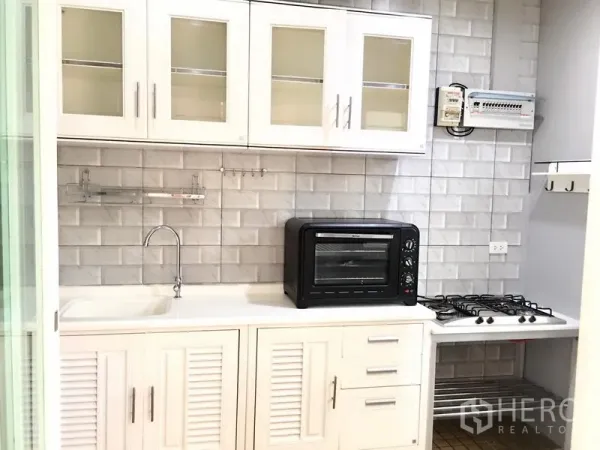 Townhouse for rent in Prawet, Bangkok - A fitted white kitchen with sink, gas hob, countertop oven and subway-tile backsplash.