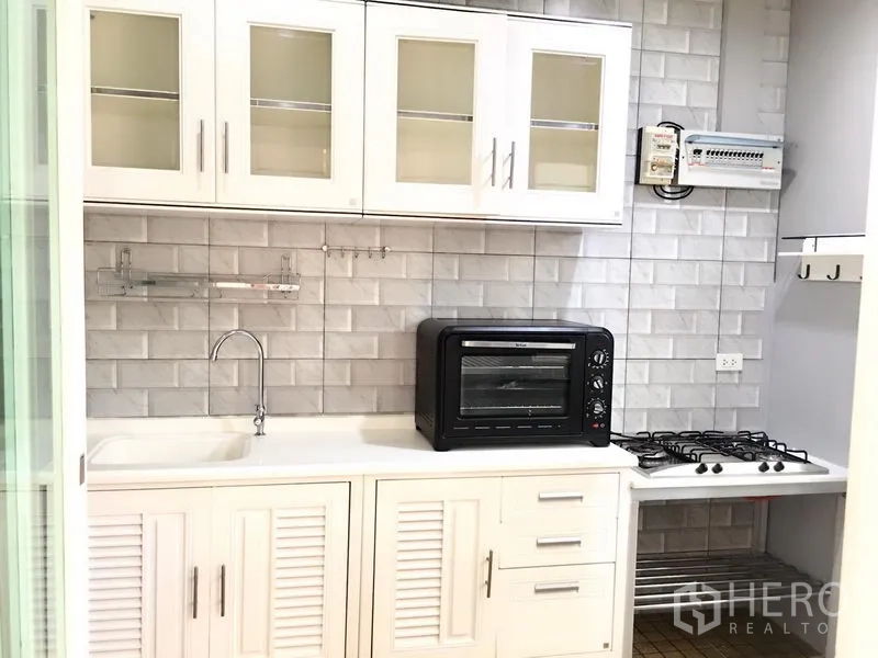 Townhouse for rent in Prawet, Bangkok - A fitted white kitchen with sink, gas hob, countertop oven and subway-tile backsplash.