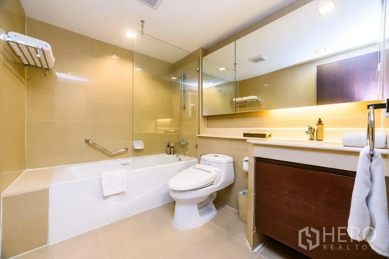 Condominium for rent in Khlong Toei, Bangkok - Bright bathroom with bathtub and glass shower screen, large mirror and vanity storage.
