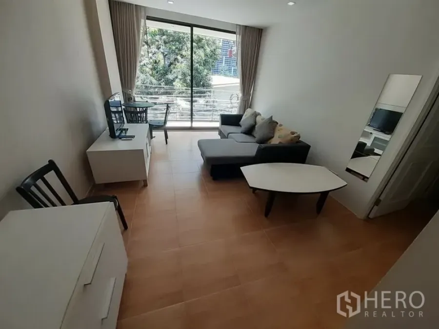 Condominium for rent in Pathum Wan, Bangkok - Bright living room with sectional sofa, TV console, work desk and large sliding glass doors to the balcony.