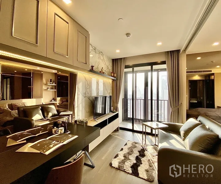 Condominium for rent in Watthana, Bangkok - Bright living room with marble TV wall, built-in shelving, work desk, and floor-to-ceiling doors opening to a balcony with city views.