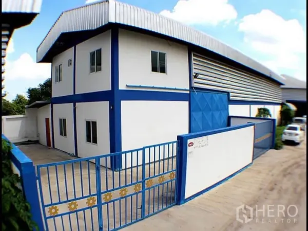 Factory for rent in Pak Kret, Nonthaburi - Corner view of two-storey office attached to factory with gated driveway and metal fence.