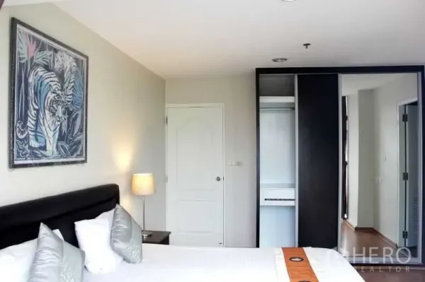 Condominium for rent in Khlong Toei, Bangkok - Primary bedroom with upholstered headboard, bedside lamp and built-in wardrobe.