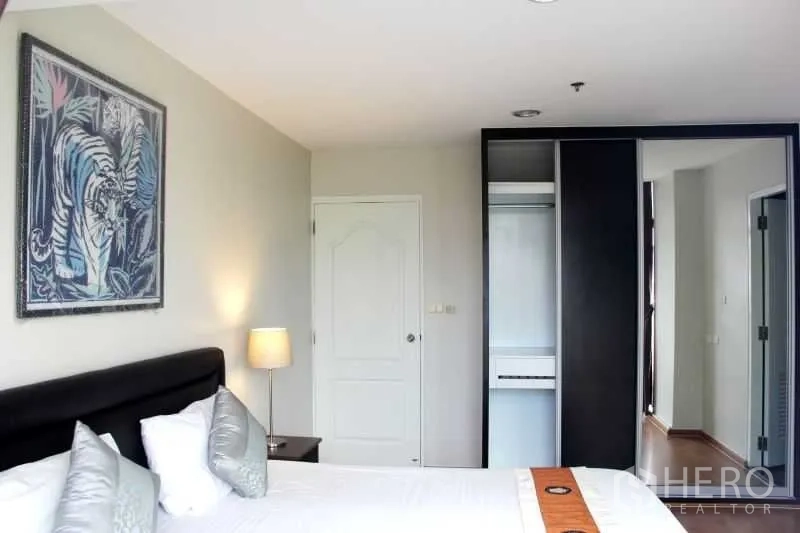 Condominium for rent in Khlong Toei, Bangkok - Primary bedroom with upholstered headboard, bedside lamp and built-in wardrobe.