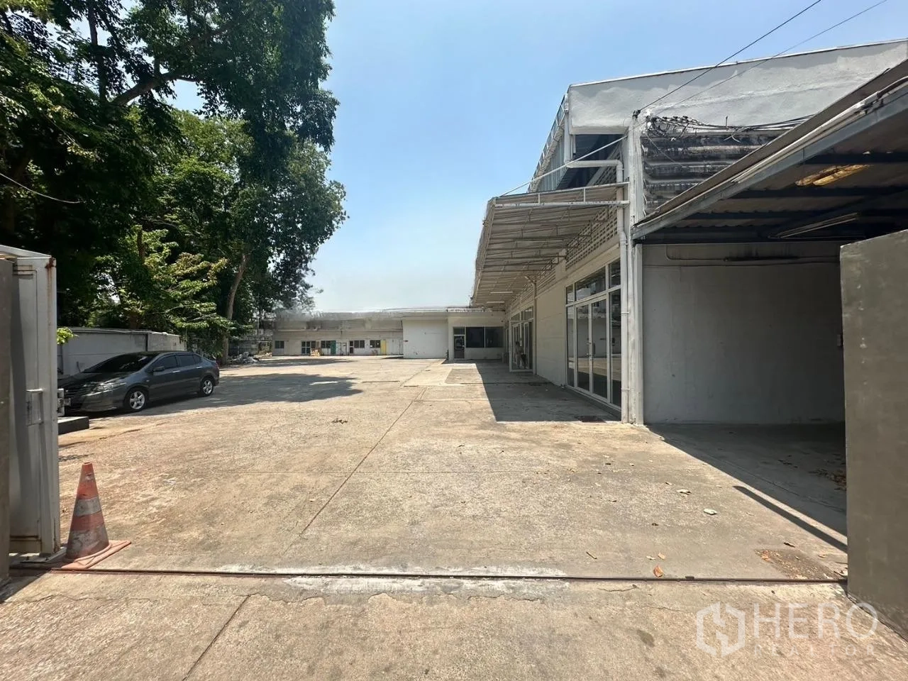 Warehouse for rent in Din Daeng, Bangkok - Driveway into the compound with shade trees, parking space, and a long warehouse facade.