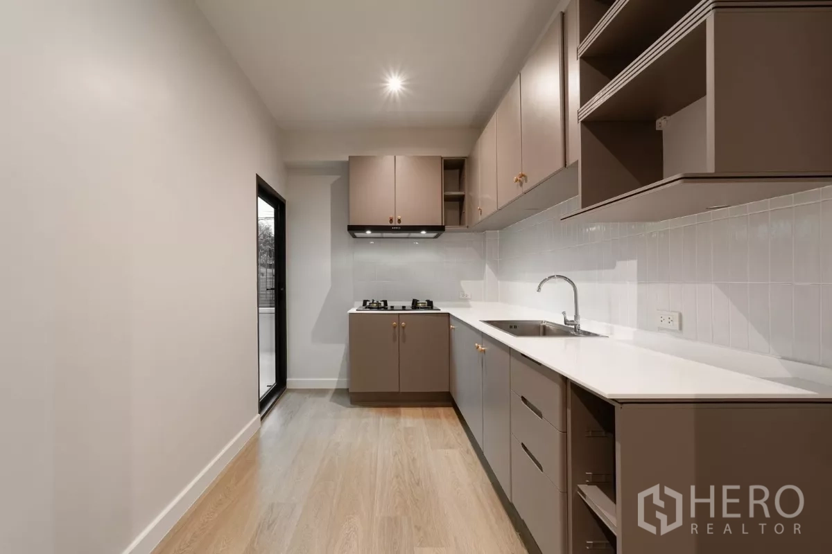 Townhouse for rent in Watthana, Bangkok - Secondary Thai kitchen with gas hobs, taupe cabinets and service balcony access.