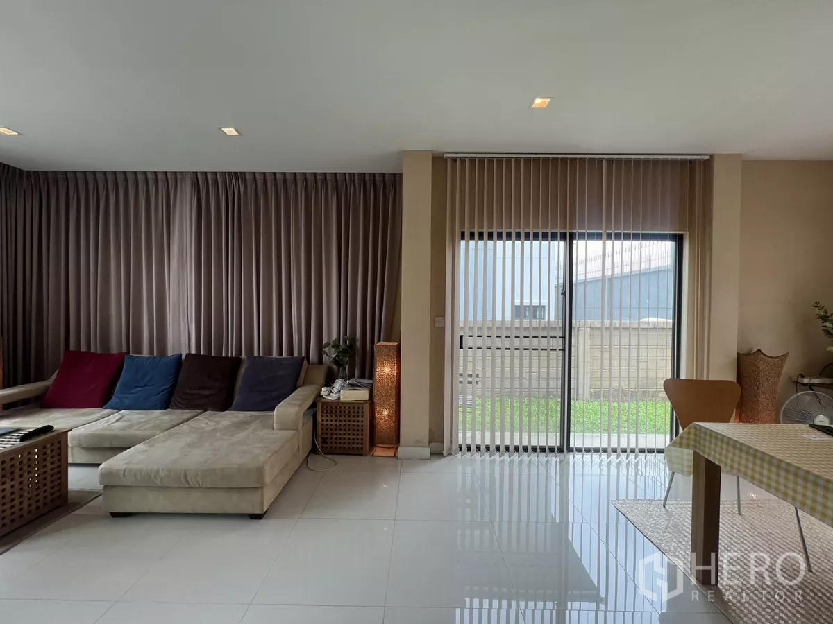 Detached House for rent in Bang Kapi, Bangkok - Lounge area with L-shaped sofa, sliding glass door, and vertical blinds.