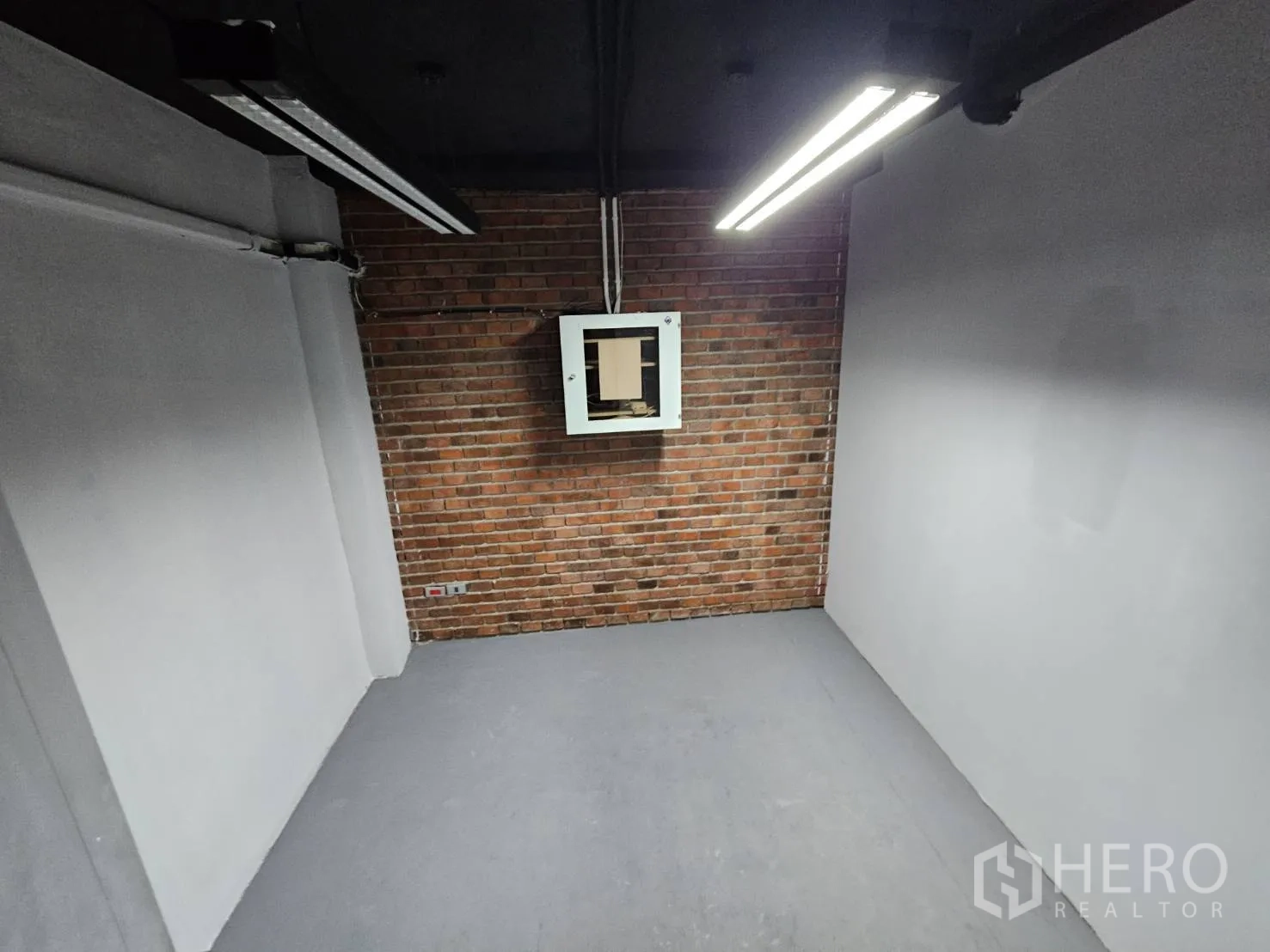 Office Space for rent in Watthana, Bangkok - Small private room with brick accent wall, black ceiling and bright strip lighting.