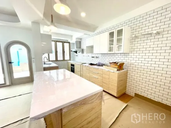 Townhouse for rent in Khlong Toei, Bangkok - Modern kitchen with white subway tile walls, wood cabinetry and a large island countertop.