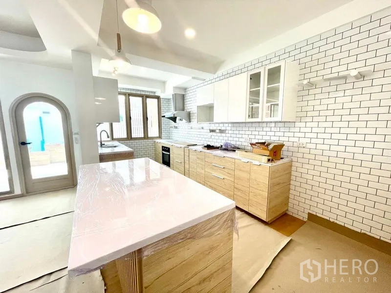 Townhouse for rent in Khlong Toei, Bangkok - Modern kitchen with white subway tile walls, wood cabinetry and a large island countertop.