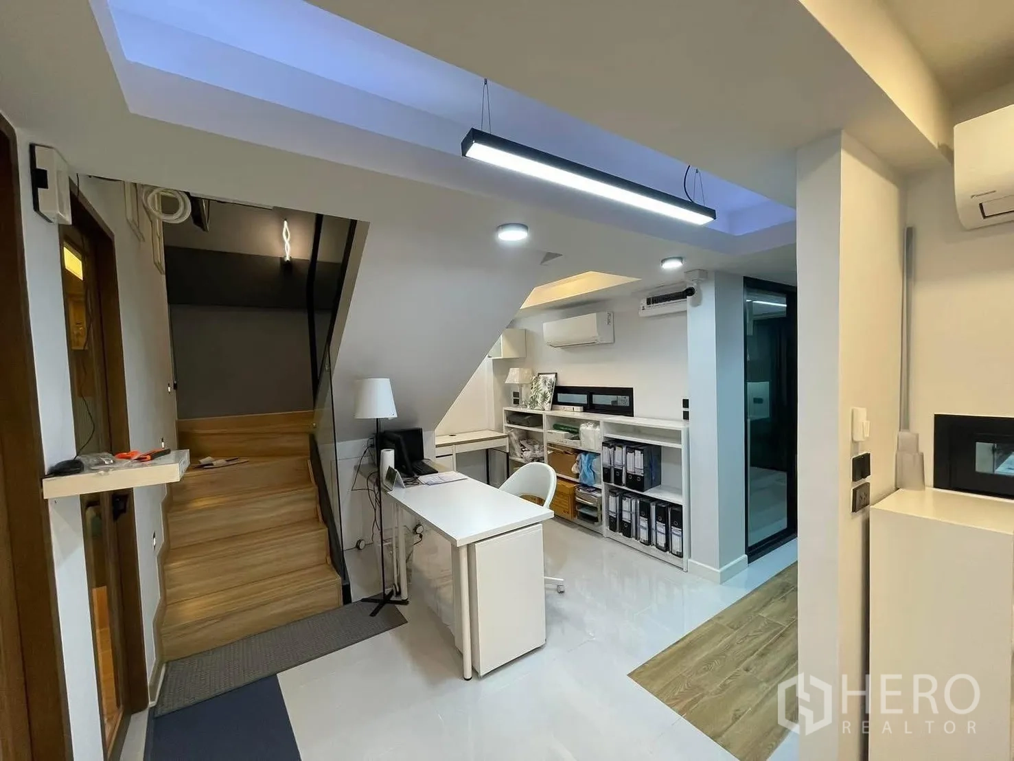 Home Office for rent or sale in Bang Kapi, Bangkok - Reception and work area beside a wooden staircase with shelving and recessed lighting.