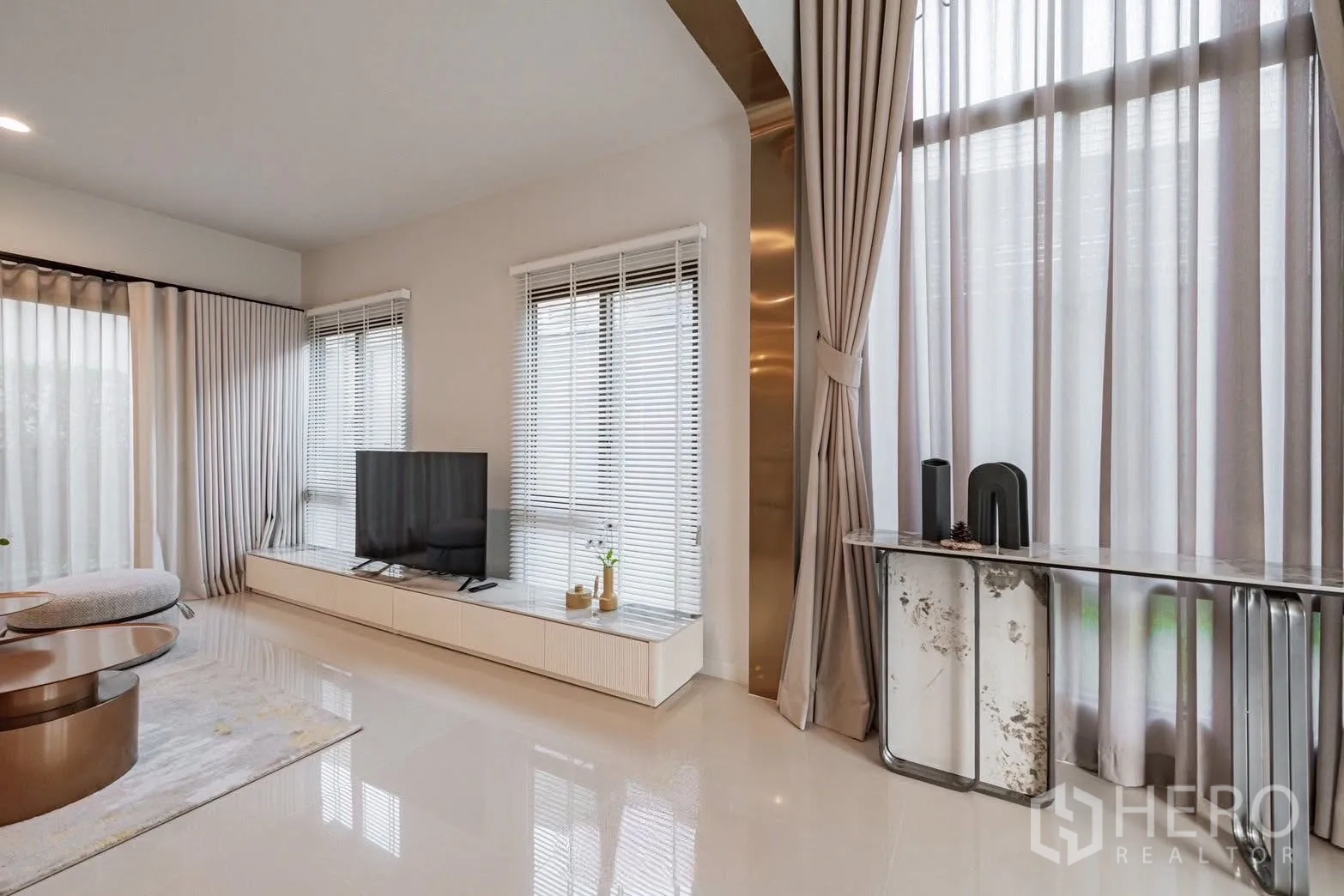 Detached House for sale in Bang Kapi, Bangkok - Living area detail showing long TV unit, venetian blinds, tall curtains and brass accent trim for a sleek finish.