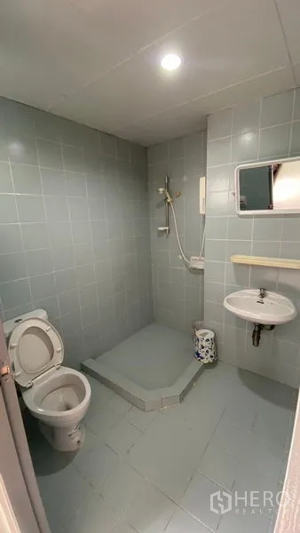 Townhouse for rent in Bang Na, Bangkok - Simple tiled bathroom with open shower, toilet and wall-mounted sink.