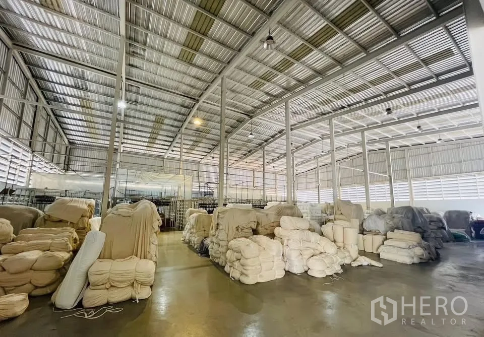 Factory for sale in Krathum Baen, Samut Sakhon - Warehouse zone with stacks of fabric rolls under a ventilated metal roof.
