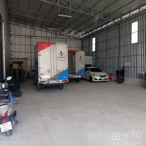 Warehouse for rent in Bang Kapi, Bangkok - High-ceiling metal warehouse interior with delivery trucks and a car parked on a concrete floor.