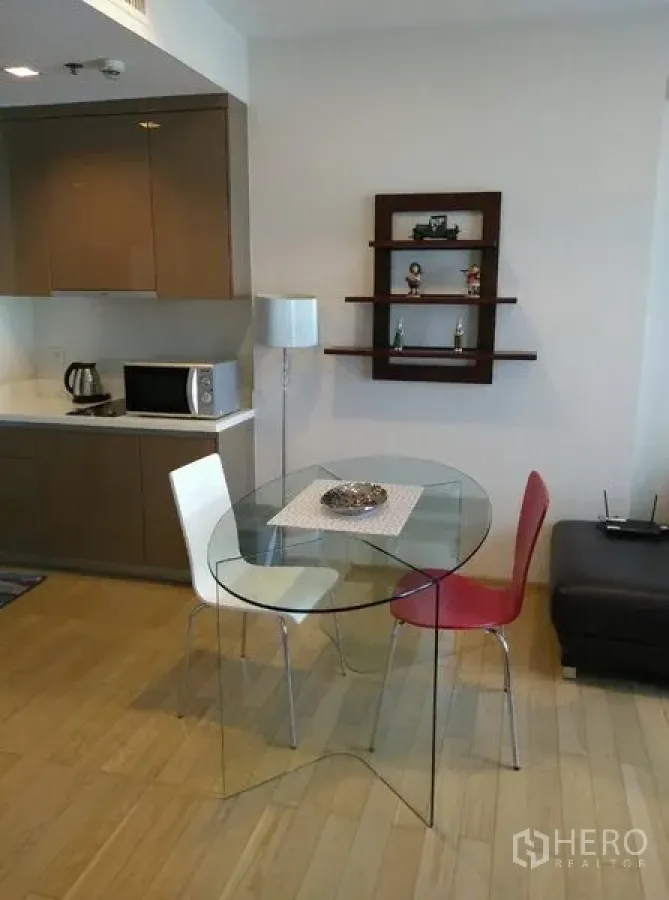 Condominium for rent in Khlong Toei, Bangkok - Open-plan dining corner with glass table for two, microwave, kettle and wall shelving beside the pantry.