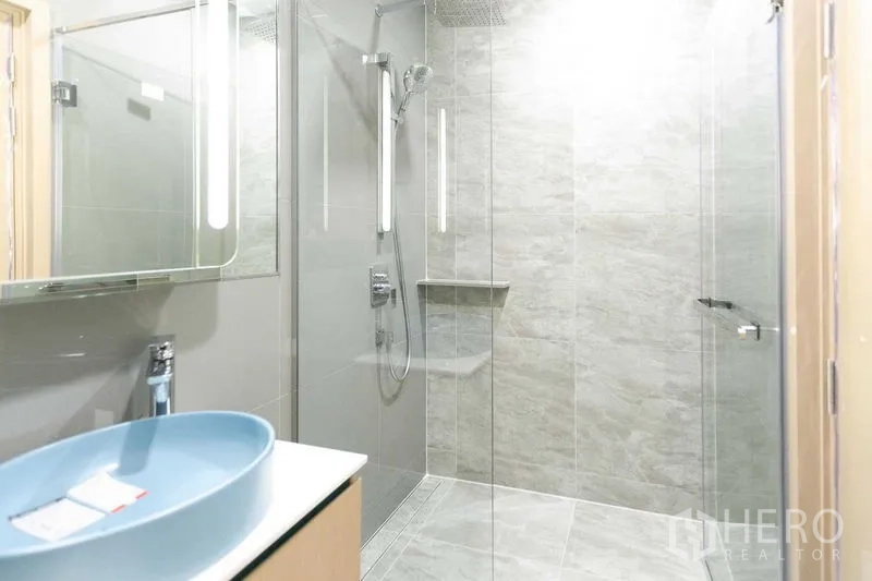 Condominium for sale in Watthana, Bangkok - Contemporary bathroom with glass‑enclosed rain shower, illuminated mirror, and gray stone tiles.