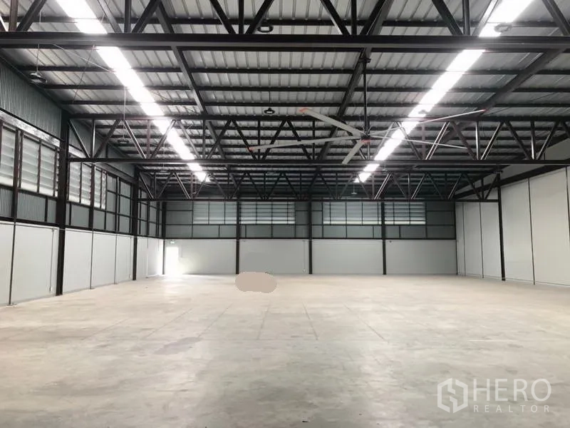 Warehouse for rent in Bang Phli, Samut Prakan - Spacious open warehouse floor with steel trusses, LED strip lighting and a large ceiling fan.