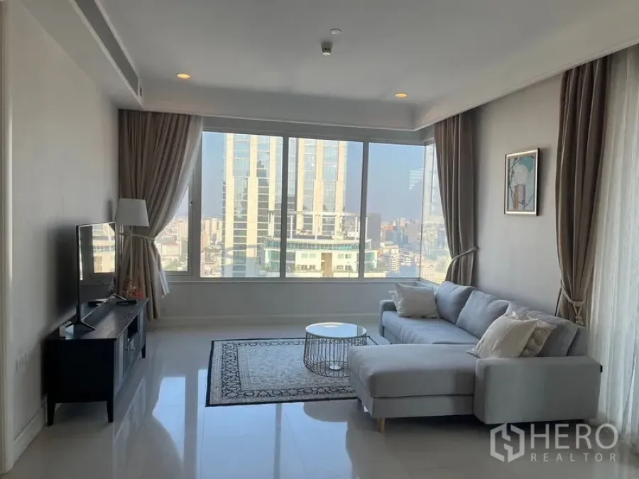 Condominium for rent in Pathum Wan, Bangkok - Bright living room showcasing large windows, an L-shaped sofa and city skyline.