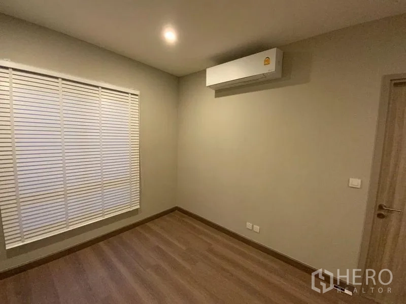 Townhouse for rent in Prawet, Bangkok - Secondary bedroom with neutral walls, wood floors and AC unit.