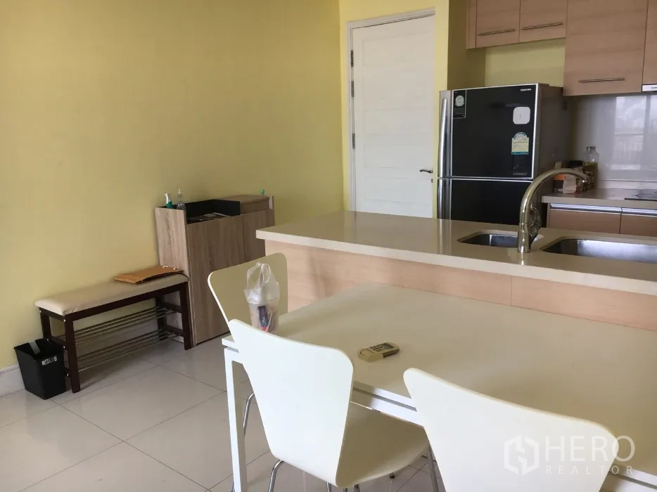 Condominium for rent or sale in Khlong Toei, Bangkok - Bright Bangkok condo kitchen with breakfast bar, double sink and stainless steel fridge beside a dining table.