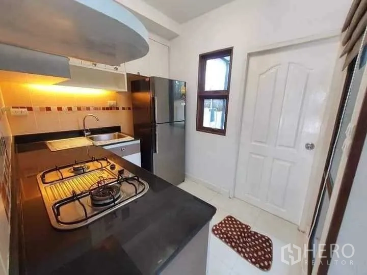 Townhouse for rent in Phra Khanong, Bangkok - Kitchen countertop with two-burner gas stove, sink and side window near door.