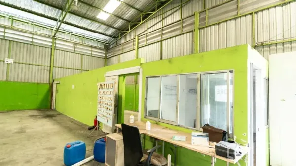 Warehouse for rent in Thanyaburi, Pathum Thani - Interior of the warehouse with a glass office booth, concrete floor and high steel roof with skylight panels.