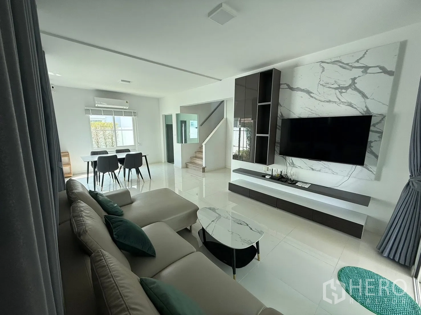 Detached House for rent in Bang Phli, Samut Prakan - Open-plan living and dining area with sectional sofa, marble-effect TV wall, and dining table.