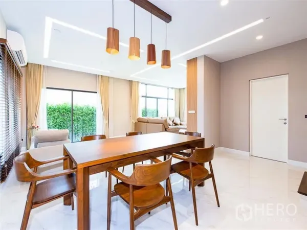 Detached House for rent or sale in Prawet, Bangkok - Bright dining area with wooden table, pendant lights and large windows overlooking greenery.